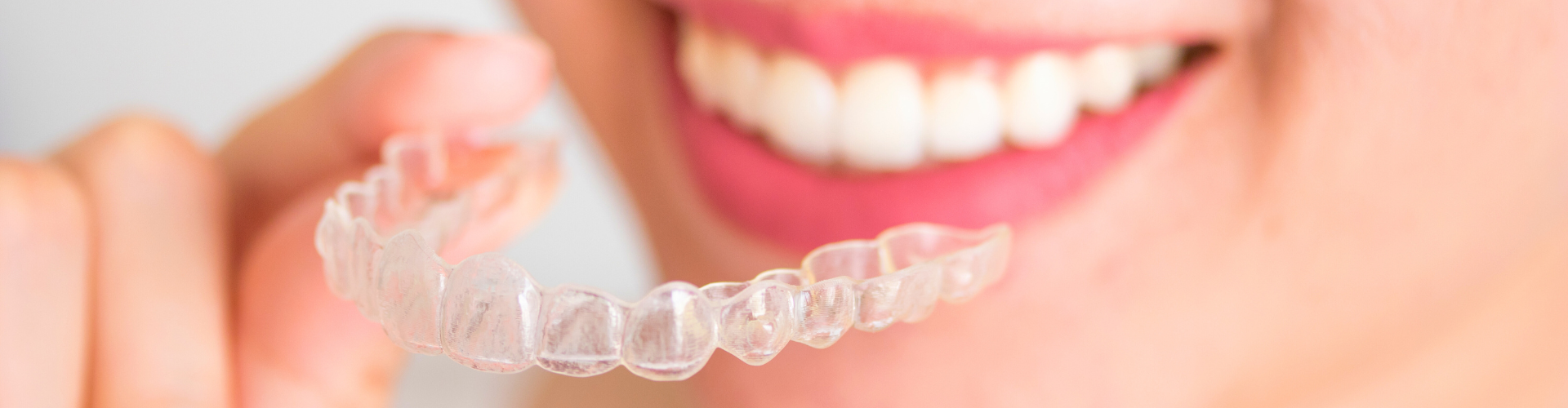 Smiling woman holding clear aligner in front of her mouth.